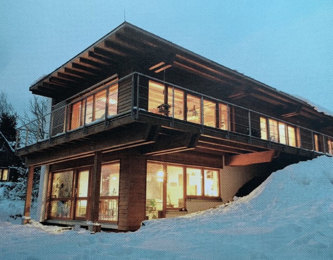 Een voorbeeld van een passief huis in schemering, in de sneeuw van hout en met ramen waar licht doorheen valt